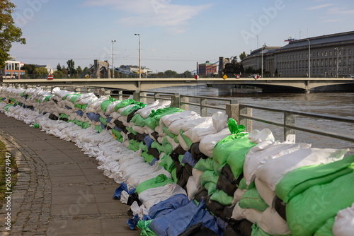 Flood defense barrier made of stacked sandbags along riverside promenade protecting nearby buildings and urban infrastructure from rising water levels during flood emergency