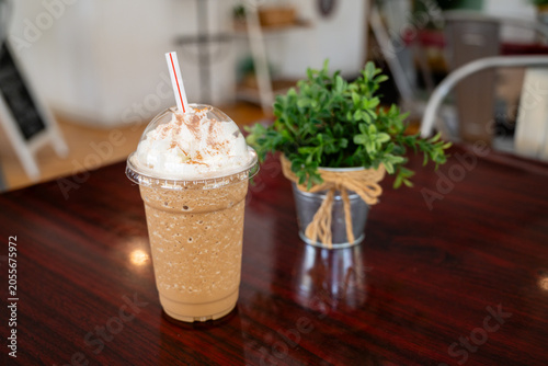 Close up of an iced coffee with whipped cream and chocolate drizzle on a wooden table at an outdoor cafe.