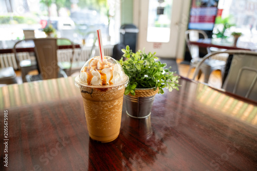 Close up of an iced coffee with whipped cream and chocolate drizzle on a wooden table at an outdoor cafe.