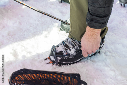 Foto Climber adjusting crampon on mountaineering boot while standing in snow before i