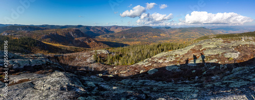 Panoramic autumn view of mountain valley with hikers' shadows on rocky summit in Charlevoix