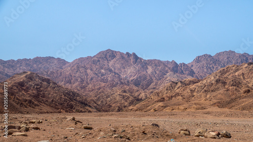 Photography Scenic view of a desert landscape with rugged rocky mountains and a highway road under a clear blue sky