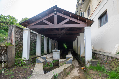 Traditional public washhouse (lavadoiro) in Viveiro, Galicia, Spain. Historic stone and timber structure with a gabled wooden roof supported by white pillars, built in October 1957.