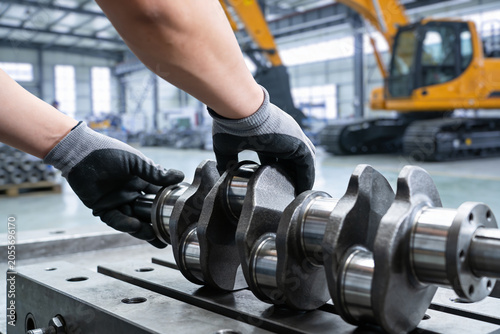 Bild auf Leinwand Mechanic inspecting a heavy-duty crankshaft in a factory setting with excavator