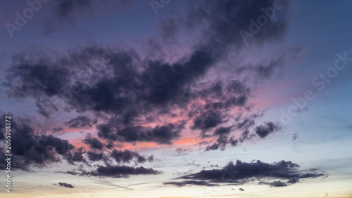 Dark dramatic clouds illuminated by soft purple and pink tones during twilight. Atmospheric evening sky with colorful cloud formations creating a moody and scenic natural background. Ideal for weather