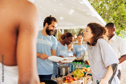 Fotografija Image shows Caucasian woman on crutches receives assistance from multicultural volunteers for hunger relief, free food and humanitarian aid provided to needy and crippled by nonprofit organization