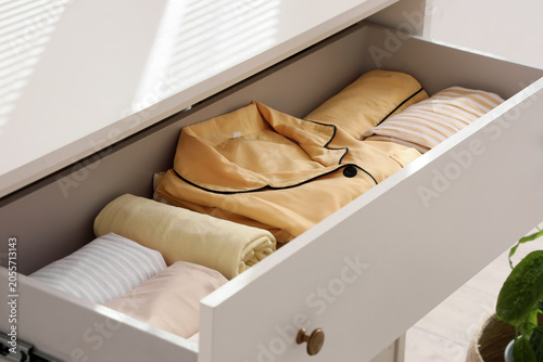 Fotografia Open drawer with neatly folded yellow pajamas and rolled clothes for organized s