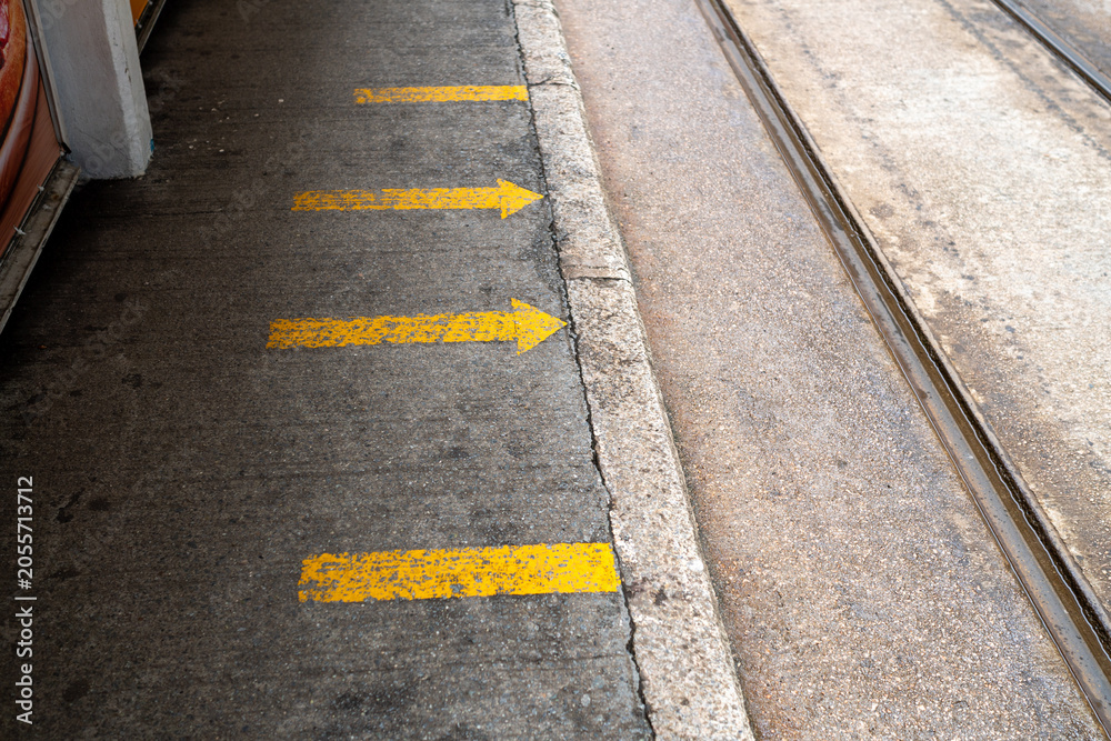 Obraz premium Yellow directional arrows painted on sidewalk at tram station platform next to tracks