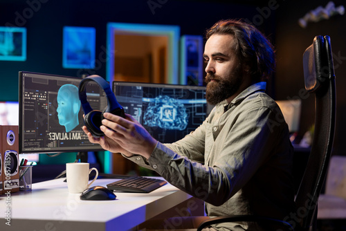 Fotografi IT specialist putting headphones on to be able to listen to artificial intelligence speaking on computer, programmer using audio device to communicate with awaken AI on PC asking existential question