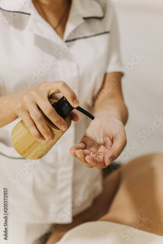 Massage therapist pouring oil onto hand in spa salon