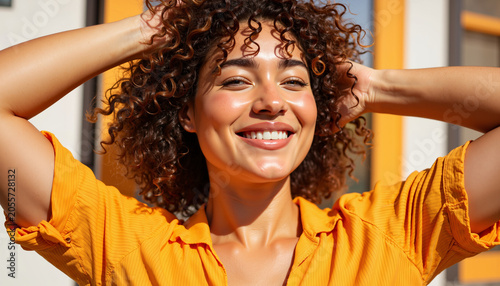 Young woman smiling with curly hair in bright orange shirt outdoors - Concept of summer mood  