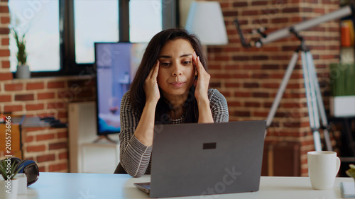 Fotografie Self employed woman feeling ill, struggling to concentrate while working from home, hurting from headache