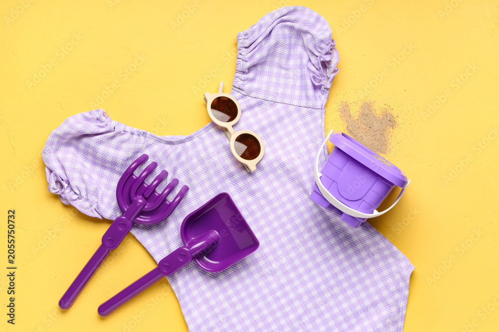 Obraz premium Childrens summer beach vacation essentials purple gingham swimsuit sunglasses sand toys and bucket on yellow background