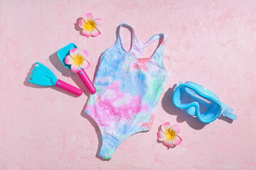Colorful tie-dye swimsuit with beach toys and diving mask on pink background, summer vacation