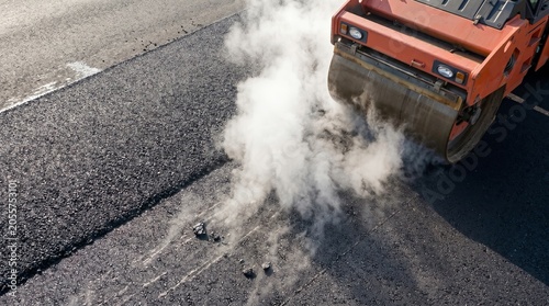 Close up of industrial road roller compacting hot steaming asphalt layer
