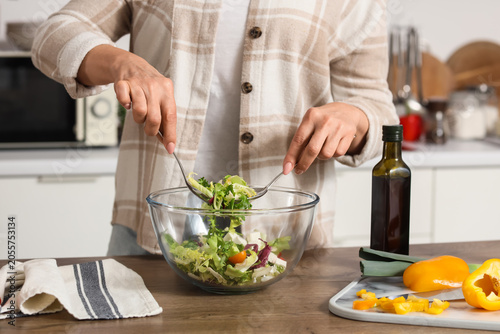 Fotografi Woman preparing fresh healthy salad in modern kitchen, mixing green vegetables a