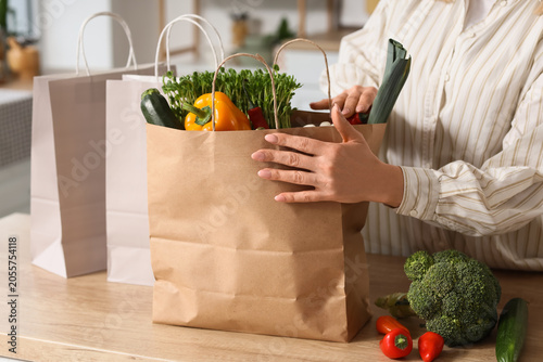 Tableau sur toile Woman unpacking fresh organic groceries from brown paper bag on kitchen counter,