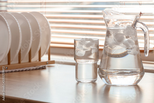 Bild auf Leinwand Refreshing cold water pitcher and glass with ice cubes on kitchen countertop by