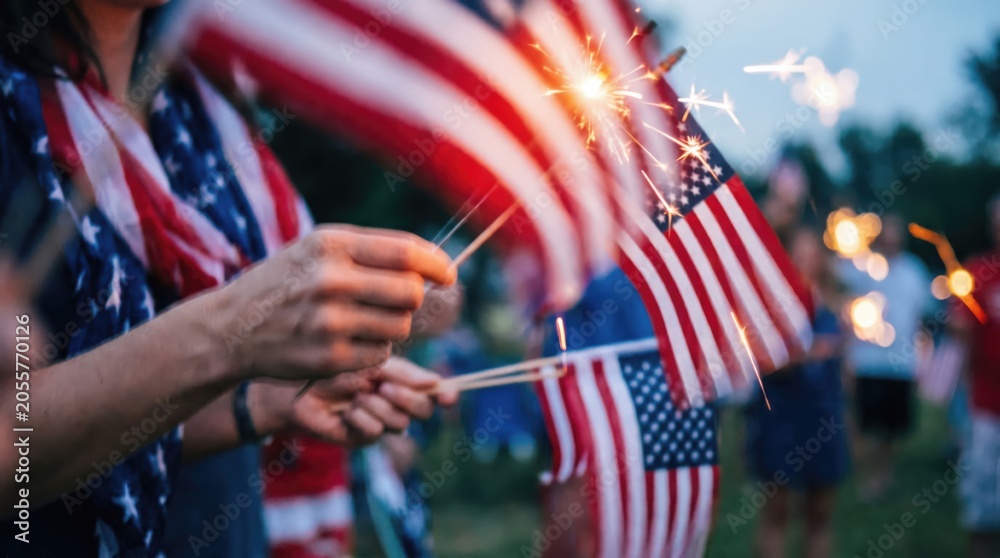 Group of diverse people holding American flags and sparklers celebrating summer holiday outdoors at dusk