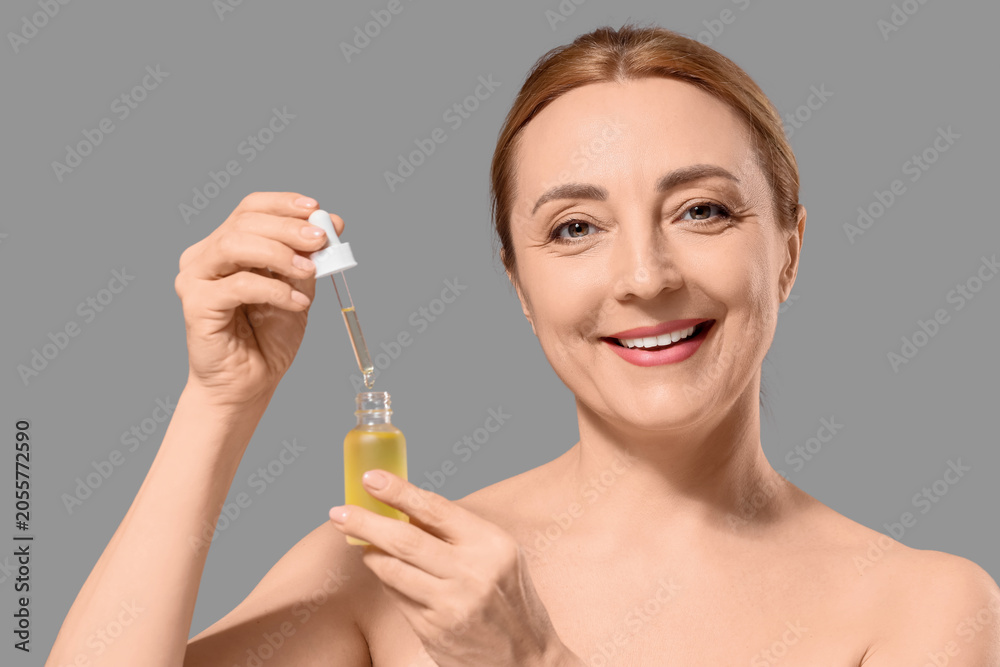 Fototapeta premium Smiling mature woman applying anti-aging facial serum for skincare routine and youthful radiance, the product is in a small bottle with a dropper, cosmetic treatment and self-care