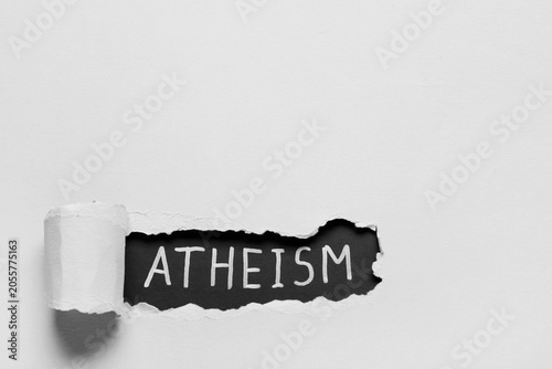Photos Atheism word revealed through torn white paper, of non-belief, skepticism, and r