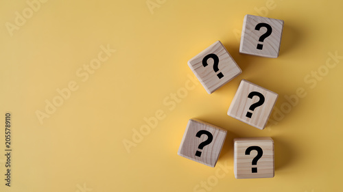 Wooden blocks with question marks arranged on a minimalist yellow background for creative problem solving concepts and conceptual thinking strategy ideas representing uncertainty