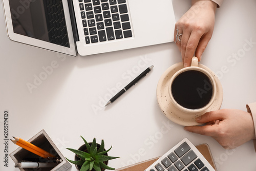 Young businesswoman with cup of coffee, calculator and laptop working at tabl...