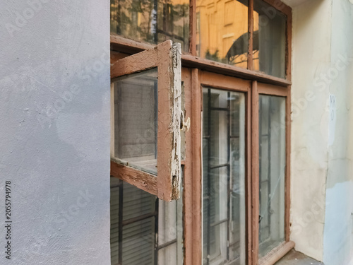 Facade of an old building with sun reflections in the windows glass. Small open leaf window, old rotten frames in the city street. Different angles