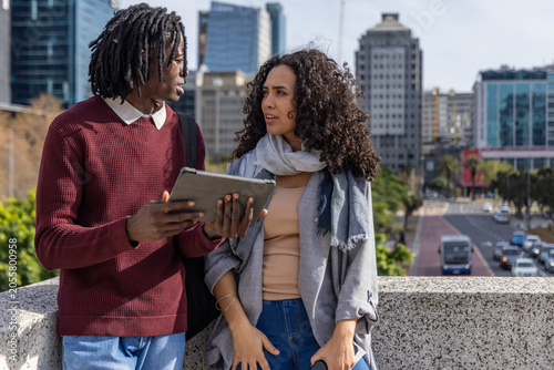 Photos Diverse friends discussing tablet, holding backpack and leaning on concrete para