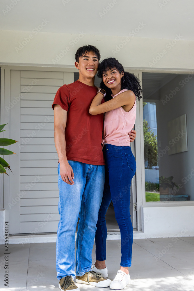 Obraz premium Diverse couple standing close on tiled porch in front of slatted door showing smartwatch