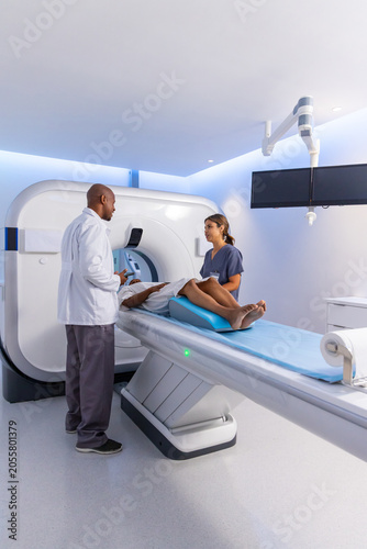 African American staff in lab coat and scrubs positioning patient on CT table with blue wedge
