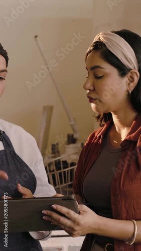 Vertical video: Tapping tablet, chef, manager checking orders at bakery rack with list, in uniform