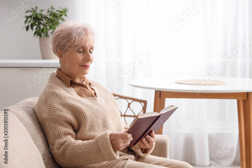 Beautiful senior woman reading book on sofa in kitchen