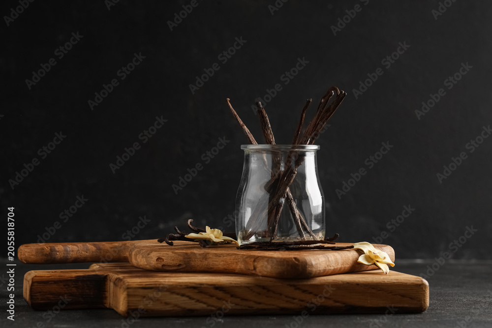 Obraz premium Glass jar with aromatic vanilla sticks and flowers on black grunge background
