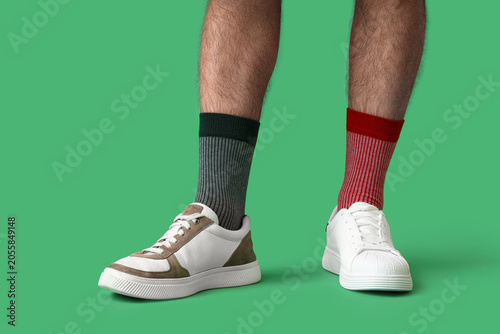 Quadro su tela Mans legs with mismatched socks and sneakers on green background, individuality