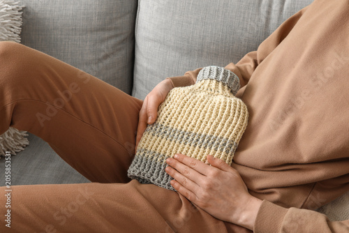 Canvas-taulu Woman warming her belly with hot water bottle on sofa at home