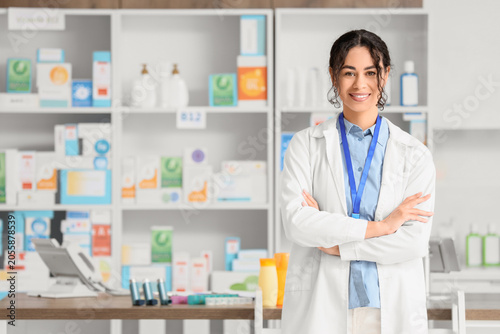 Smiling female pharmacist in white lab coat standing with folded arms in mode...