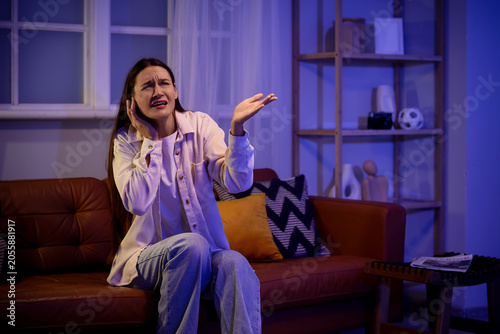 Young woman on sofa suffering from noisy neighbours at home late in evening