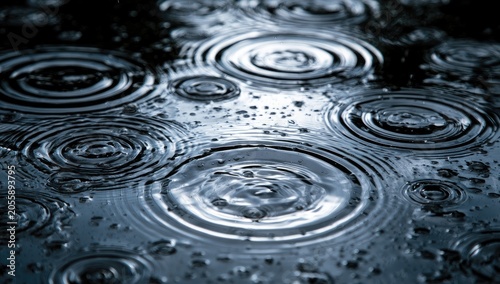 Close-up of raindrops hitting a dark, reflective surface, creating ripples