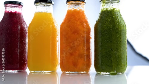 Row of colorful cold pressed juices in glass bottles with condensation droplets on white background