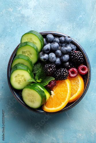 Fresh fruit and cucumber salad in a decorative bowl on a blue background