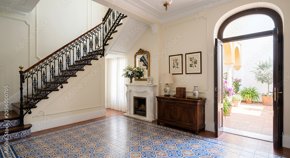 Obraz premium An elegant entryway features a grand staircase with ornate iron railings, a marble fireplace, and a patterned tile floor. 