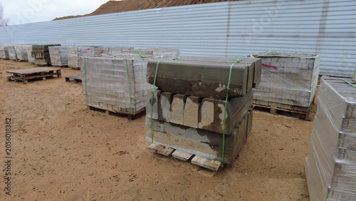 Pallets stacked with concrete materials are lined up in a construction site during the day near a storage area
