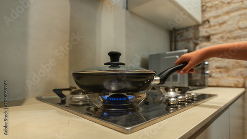 Child's hand holding a frying pan on a gas stove with a blue flame