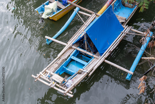 A high-angle view of a traditional blue wooden outrigger boat with a blue canopy docked on the water in Cilacap, Indonesia.