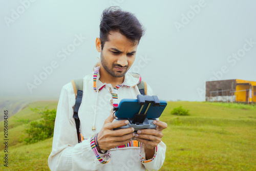 Photography Young Man Using Smartphone with drone controller on a Misty Hilltop, Banswara, U