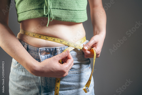 Foto Woman measuring her waist with a tape measure on a gray background