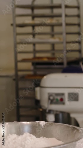 Vertical video: Entering left baker in apron dusting flour at bakery reaching mixing bowl for dough