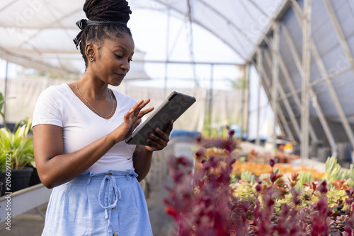 Fotografia African American woman wearing white tee, checking tablet folio case among succu