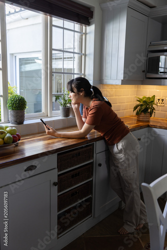 Smartphone resting on wooden countertop undercabinet lighting with bowl of apples at window